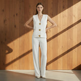 Woman wearing a white vest with gold buttons and matching pants on a gray background