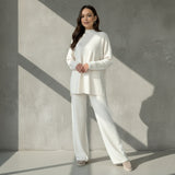 Woman wearing a white outfit standing against a gray wall