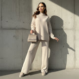 Woman in a beige outfit holding a matching handbag against a concrete wall.