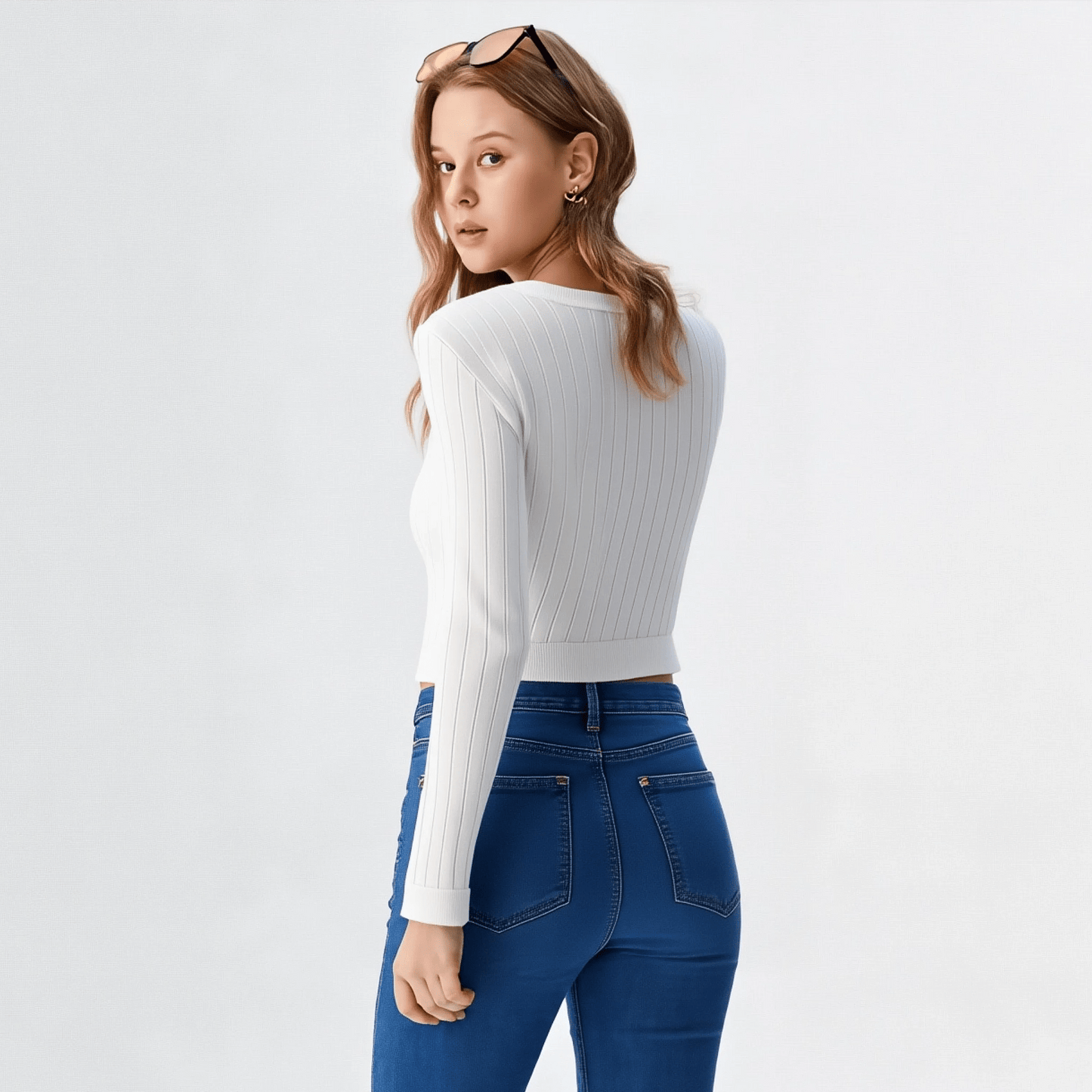 Woman wearing a white long-sleeve top and blue jeans on a light gray background