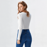 Woman wearing a white long-sleeve top and blue jeans on a light gray background