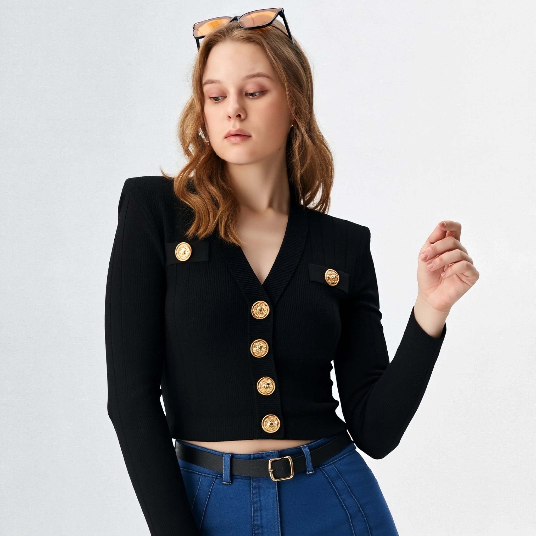 Woman wearing a black blazer with gold buttons and blue jeans on a light gray background