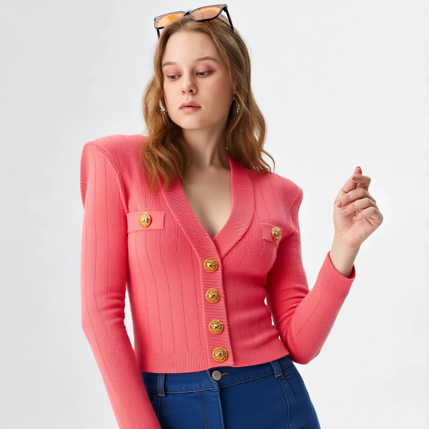 Woman wearing a pink cardigan with gold buttons on a light gray background