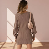 Woman wearing a brown ribbed dress holding a beige handbag against a plain background